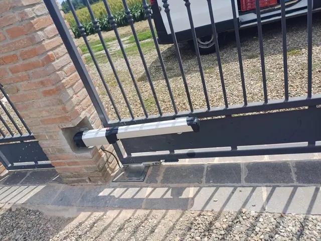 Attuatore lineare montato sull'anta di un cancello a battente accanto al pilastro in mattoni