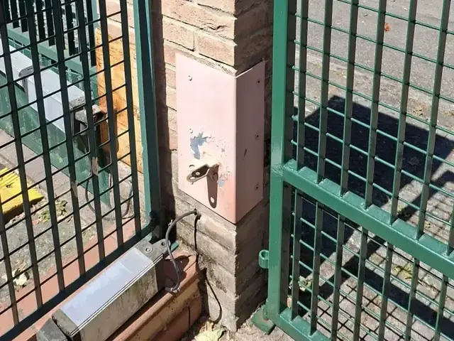 Attuatore fissato al pilastro di un cancello verde a doppia anta