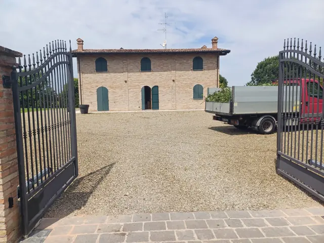 Cancello automatico a battente aperto sul cortile di un casale in mattoni