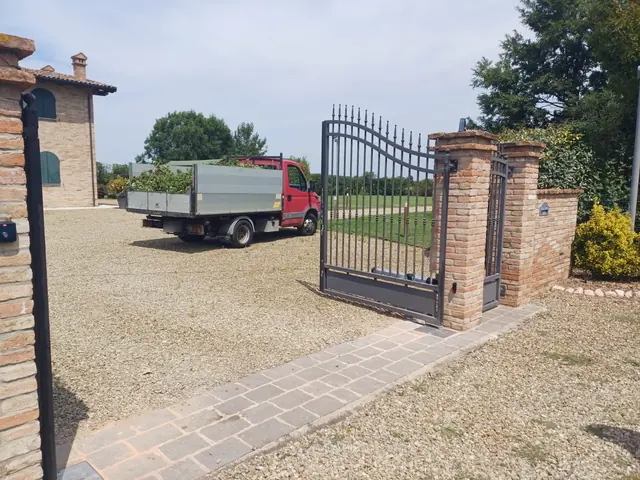 Anta di un cancello automatico a battente aperta sul cortile, con pilastri in mattoni